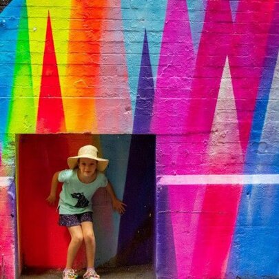 A child posing in an alcove in a rainbow mural.