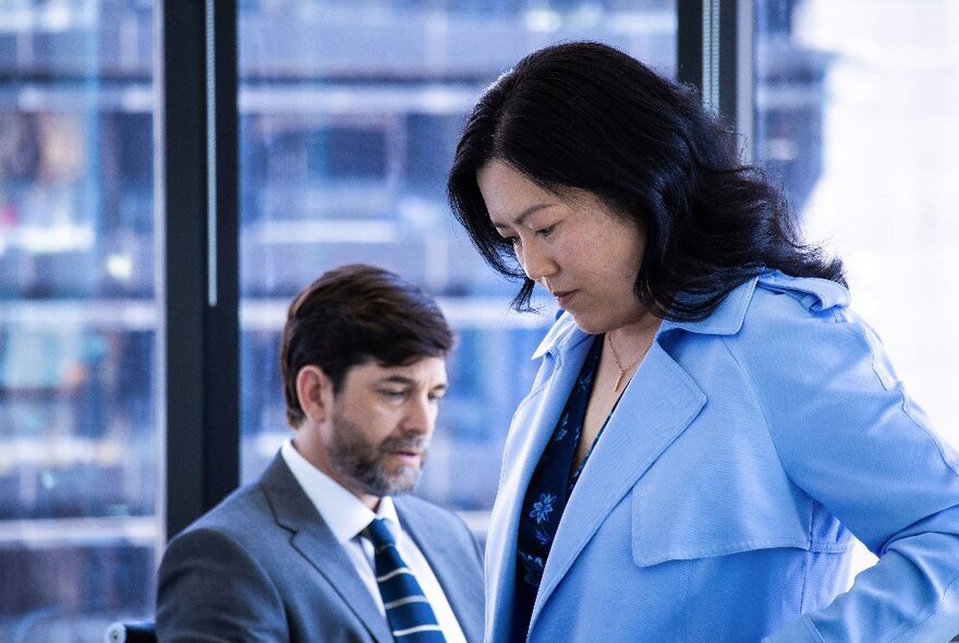 Woman wearing a blue coat next to a seated man and refrigerated drinks cabinet.