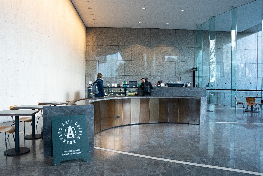 The curved coffee counter of Axil Coffee at number 1 Spring St, with glossy marble floors, and a few tables and chairs close by.