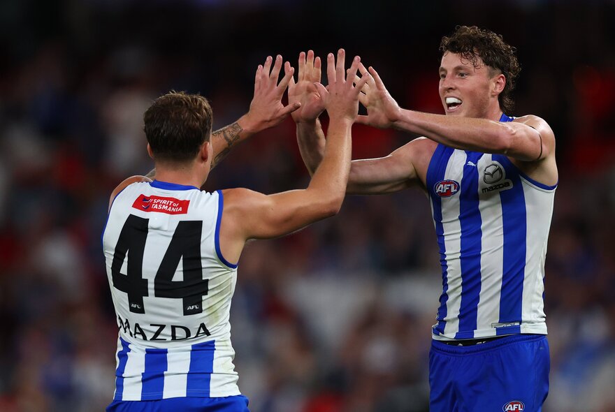 Two North Melbourne players high-five on the field. 
