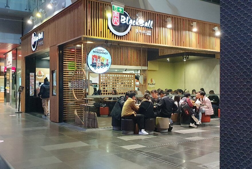 Shopfront exterior of BlackBall showing patrons seated on low stools out the front.