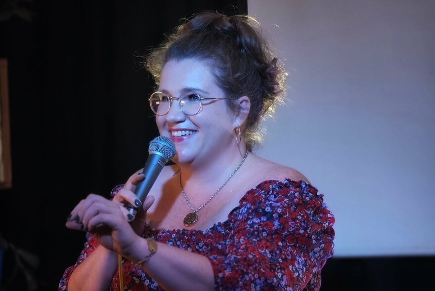 Woman performing with microphone on stage, smiling.