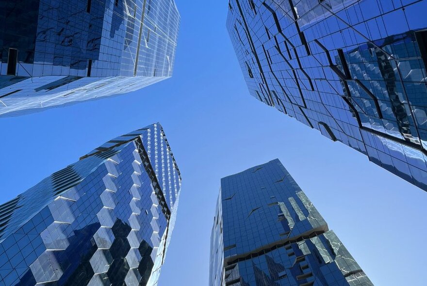 Looking up through the sky to the tops of four towering skyscrapers.