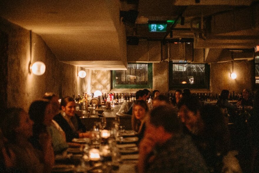 People seated at a candle-lit long table in a dimly lit restaurant.