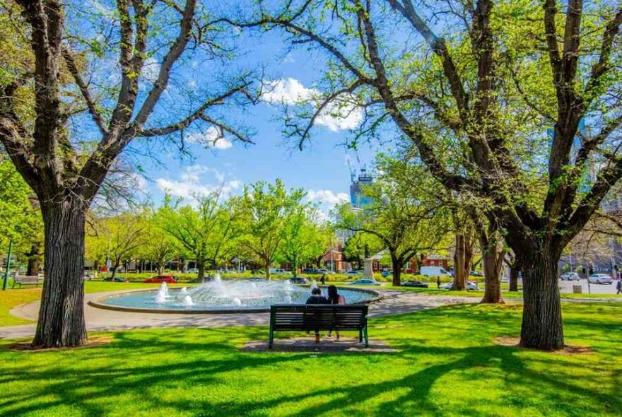 Two people sitting at a park bench in a garden