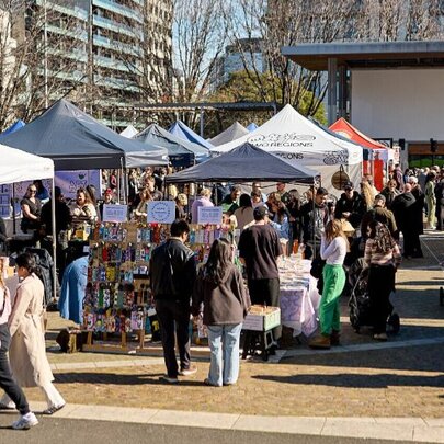 Outdoor market with tented stalls, strolling marketgoers, bare winter trees and city buildings.