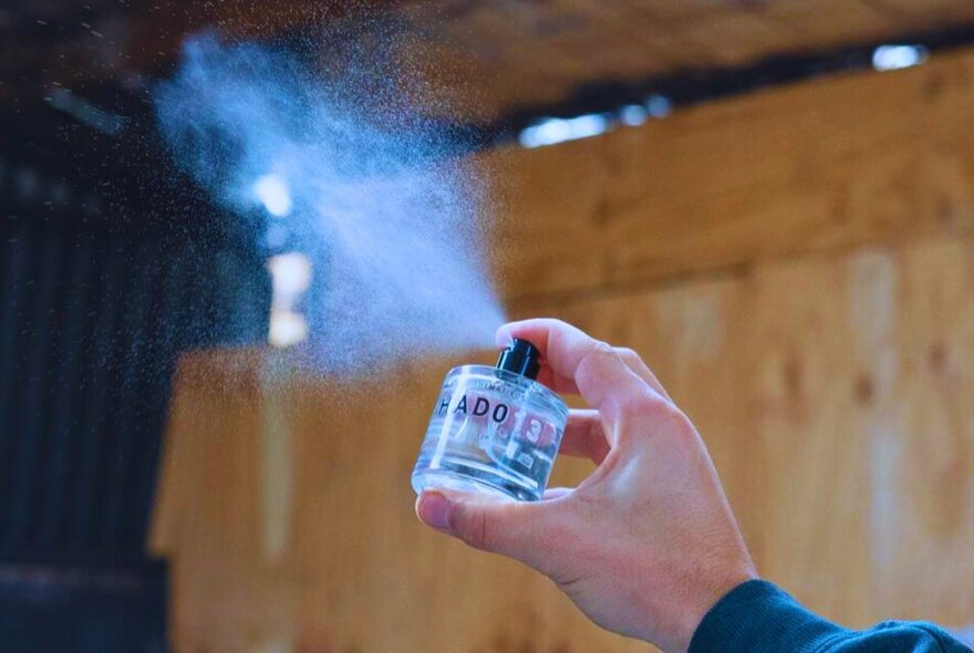 A hand spraying perfume from a small bottle into the air, at a perfume making workshop.