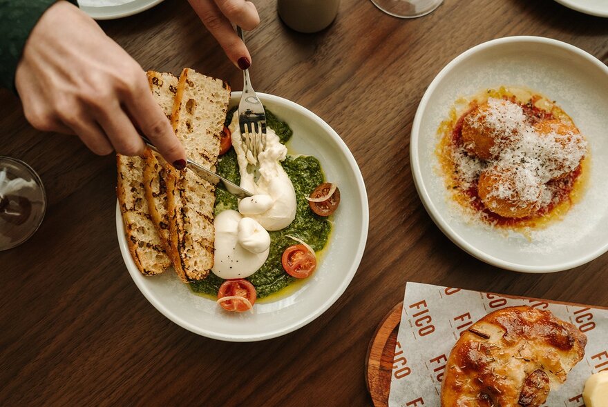 Overhead view of a fresh Caprese salad plate next to a flatbread pizza on a marble table.