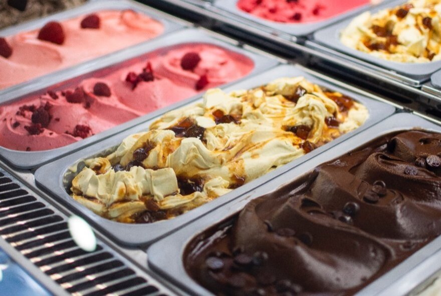 A selection of four colourful gelato tubs in a fridge each with toppings.