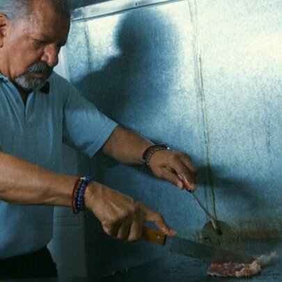 A man in a blue polo shirt cooking steak on a large griddle in a chef's kitchen.