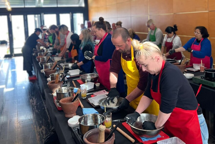 People wearing bright aprons working at long counters preparing cooking ingredients.