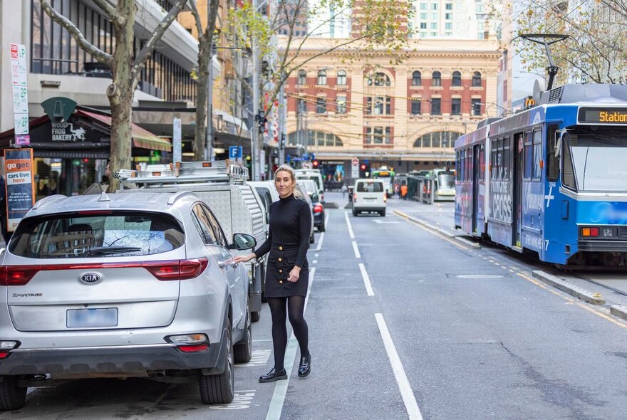 Women getting into a parked car while a tram passes by on the road.