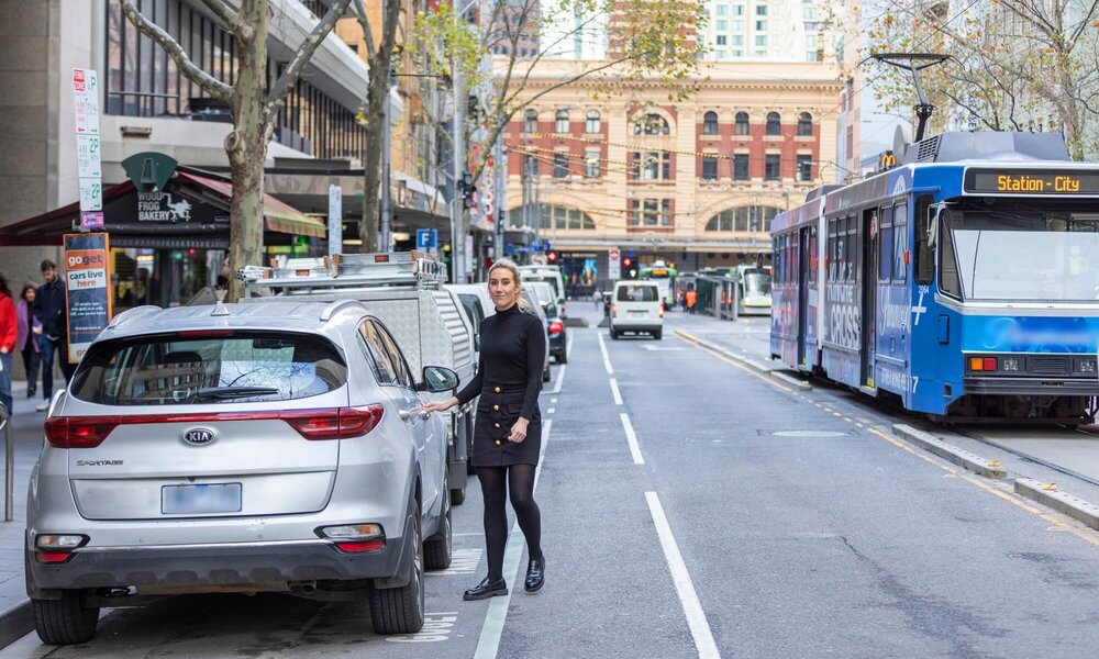 Women getting into a parked car while a tram passes by on the road.