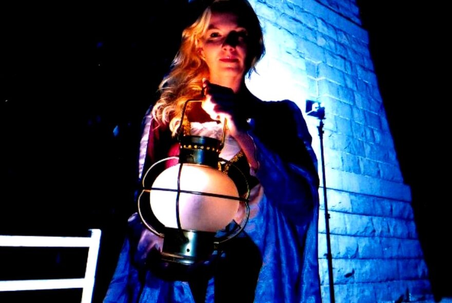 Woman posing with an old-fashioned lantern in a brick-lined alley, wearing a cape.