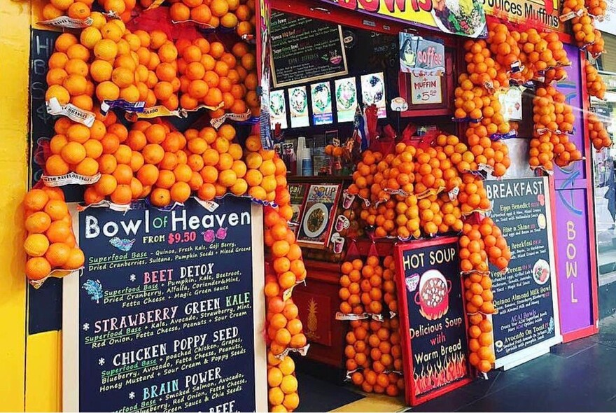 Close up of shopfront, with bags of oranges and blackboard menus around entrance.