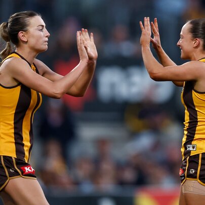 Two Hawthorn Hawks AFLW players giving each other a double high five in celebration during a game.