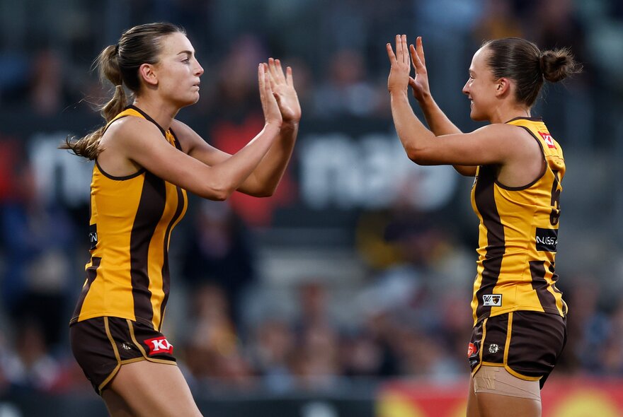 Two Hawthorn Hawks AFLW players giving each other a double high five in celebration during a game.