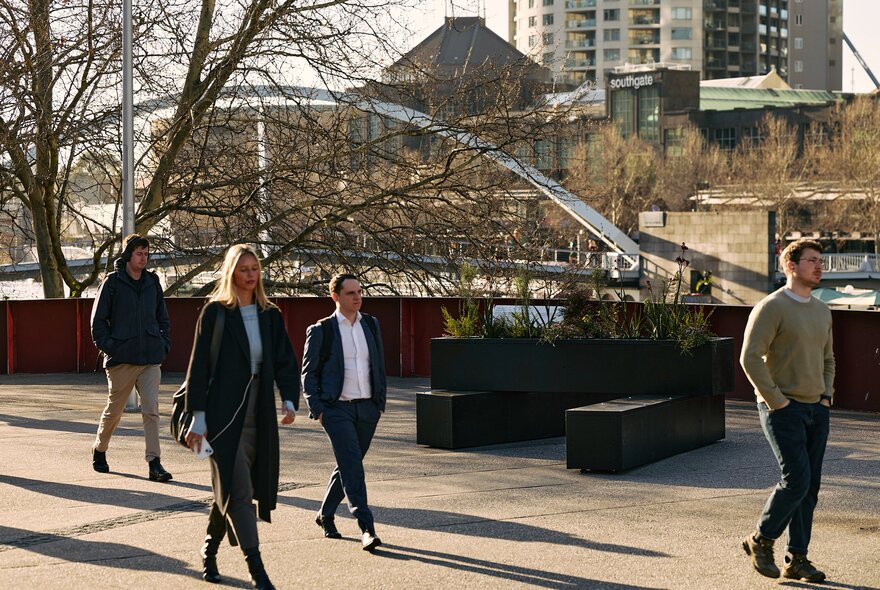 People walking past a public art installation in Melbourne with long planter pots and ferns. 