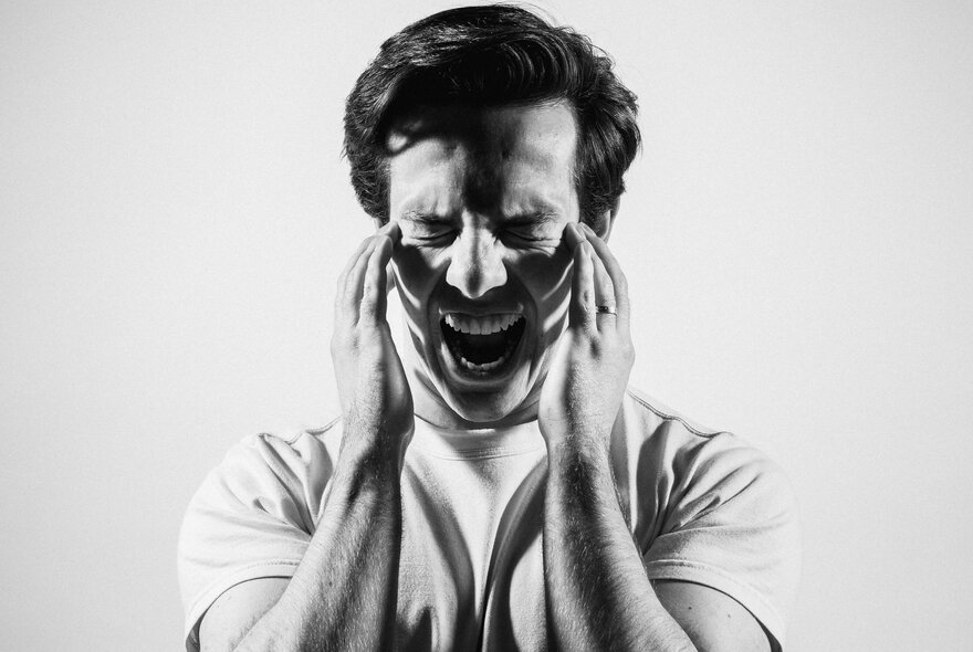 A black and white image of a young man screaming and holding his face.