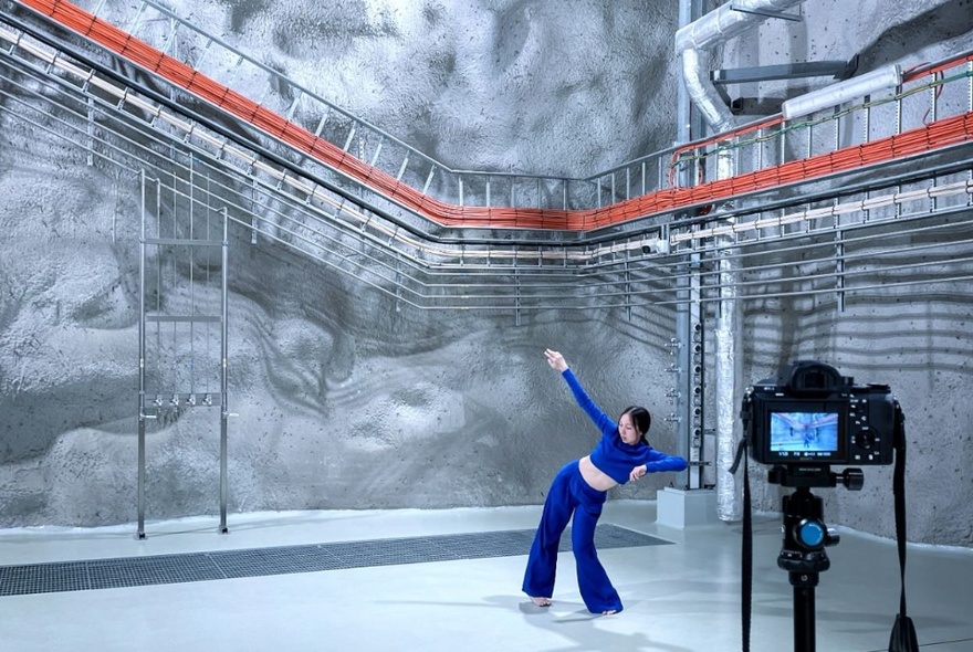 Person being filmed while moving, as if dancing, in a large room or exhibition space. 