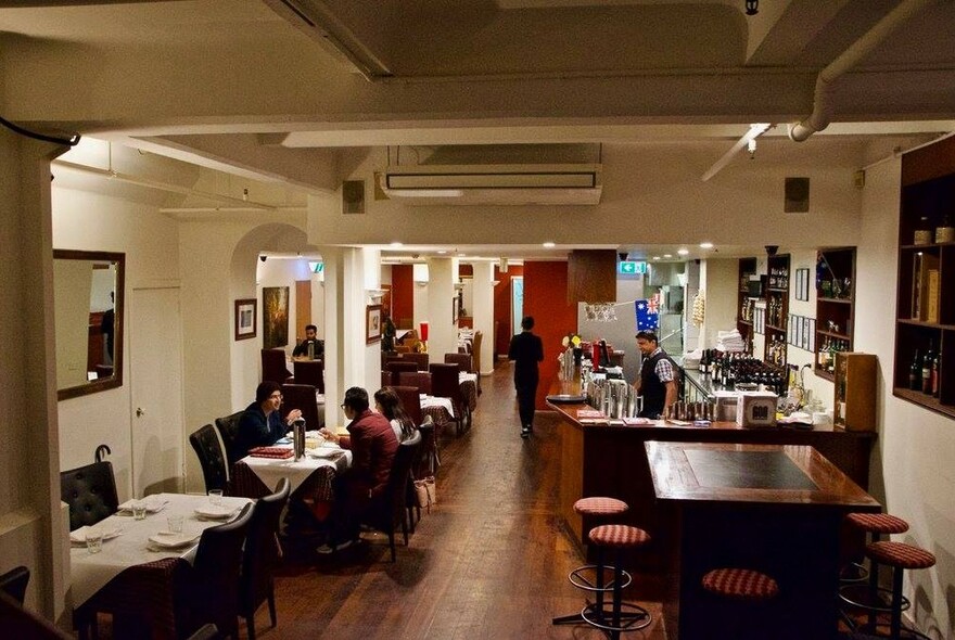 Curry Vault interior with tables with diners and staff, white tablecloths on one side of the room and a wooden bar on the other.