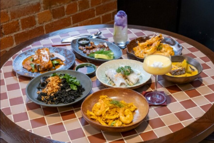 Thai dishes of food on a tiled table with drinks.