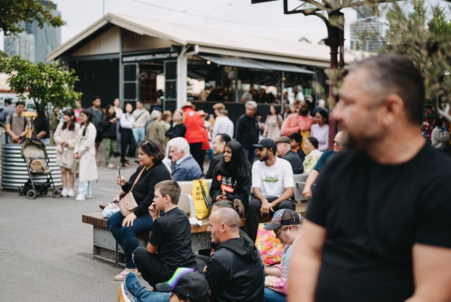 A gathering of people in an outdoor setting, near the sheds at Queen Victoria Market.
