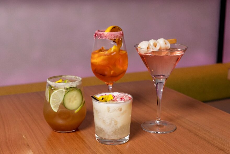 Four cocktails in variously shaped glasses lined up on a table.