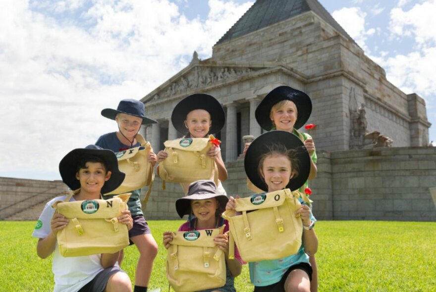 Kids on the grass outside the Shrine of Memorial, holding kit bags and smiling.