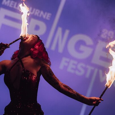 A woman eating fire from sticks with Fringe Festival lettering in the background in blue. 