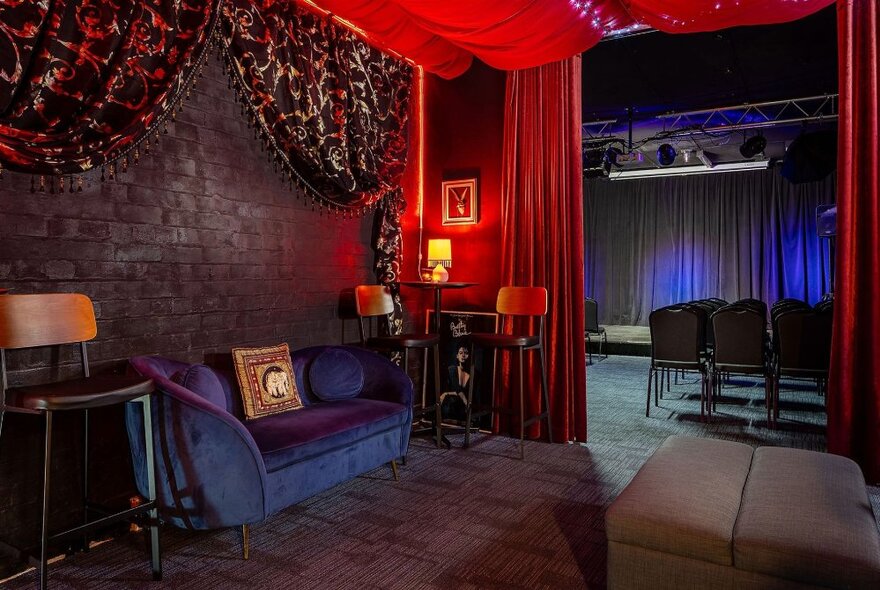 The lobby of a comedy venue, with a blue velvet couch and red curtains.