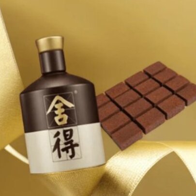 A traditional brown and cream-coloured Chinese Baijiu bottle with chinese characters next to a block of unwrapped chocolate and gold ribbons.