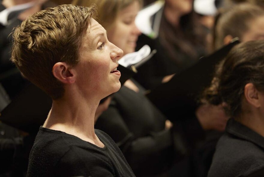 A choral singer in black with other members of the choir behind her.