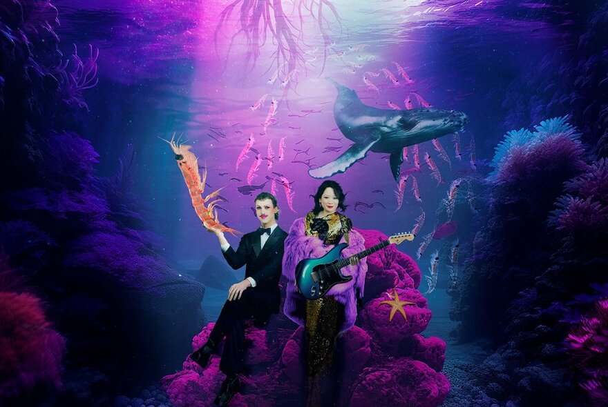 Fantastical underwater scene with two people seated on a coral rock formation, one holding an electric guitar, with a whale and fish swimming around.