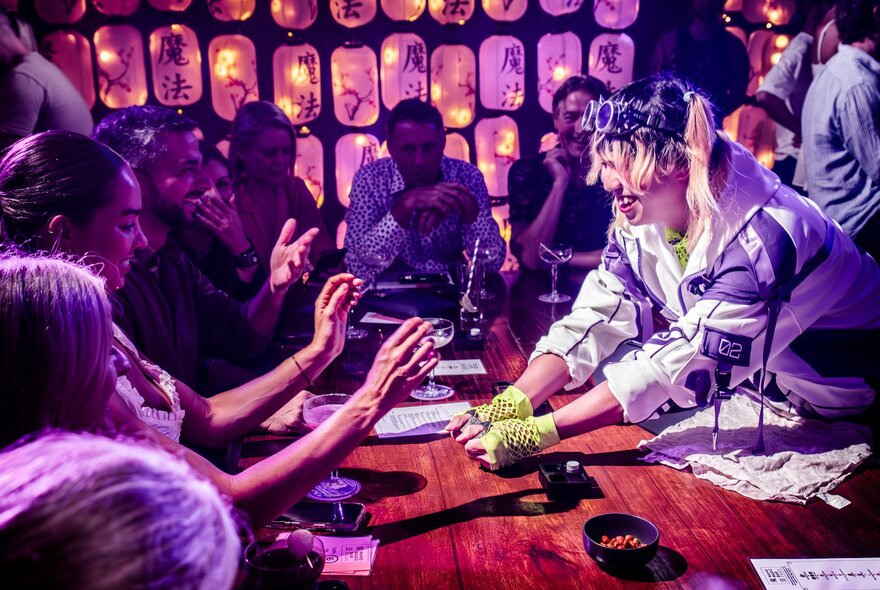 Performer with hands oustretched to seated people interacting over table.