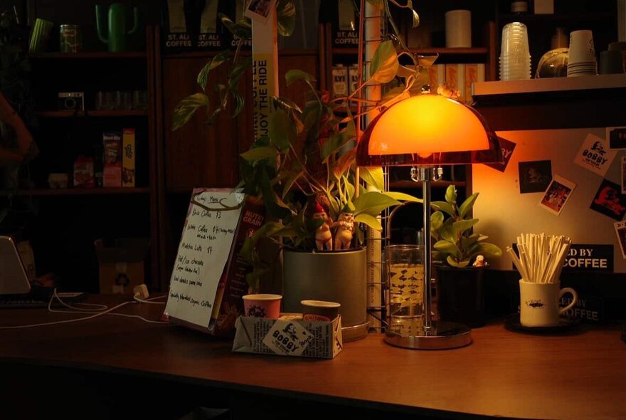 A dimly-lit room with an orange glowy half dome light on a desk. 