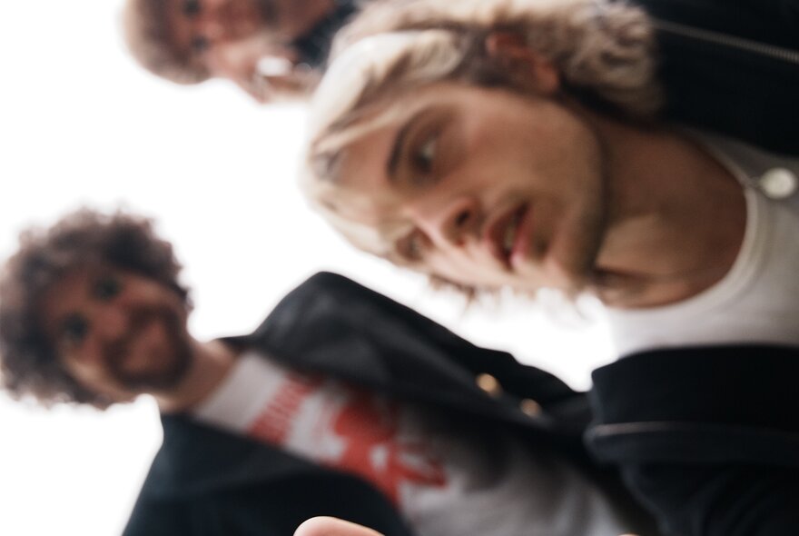 A blurry shot of three members of the band Seven Pound Halo, looking down toward the camera against a bright, overexposed white background.
