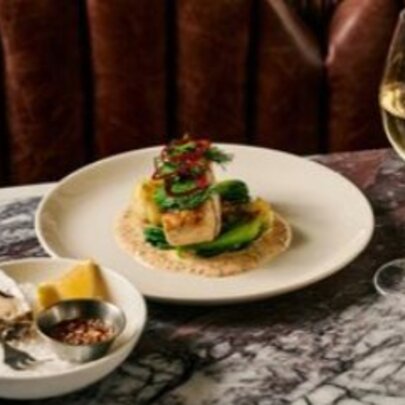 Dish of oysters and plate of food with glass of wine on a marble table.
