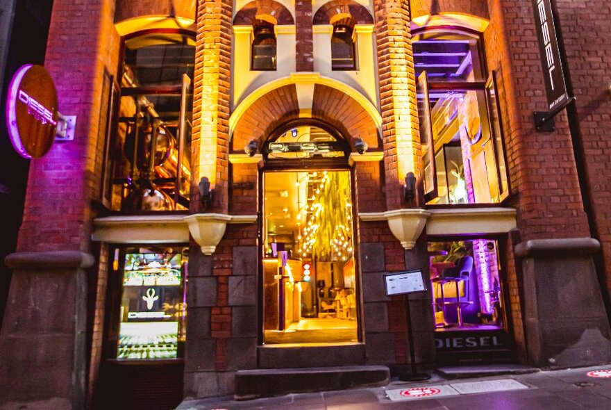 Exterior view of bar lit golden inside, with neon pink shingle.