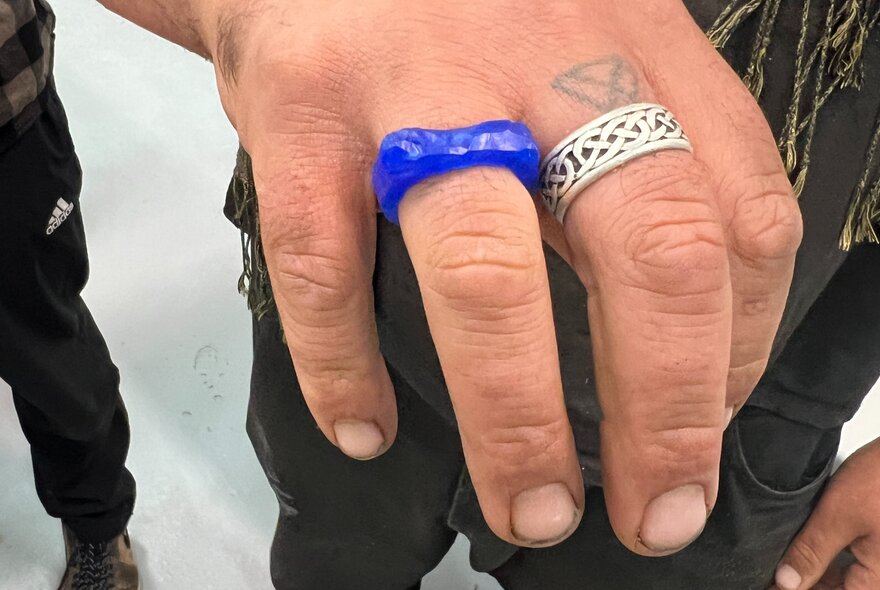 A hand with a silver ring on the middle finger and a blue ring made from jewellers' wax on the ring finger.