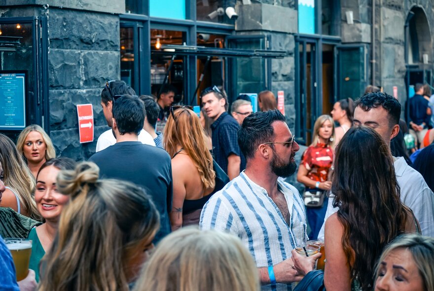 People gathered outside an old bluestone building holding drinks.