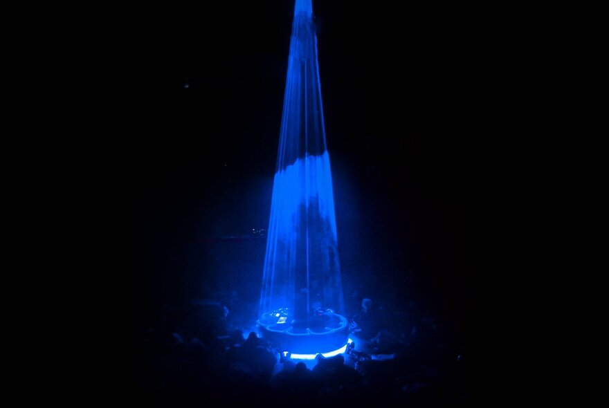 A blue cone spotlight used during a live performance, creating a dramatic effect in a dark environment. 