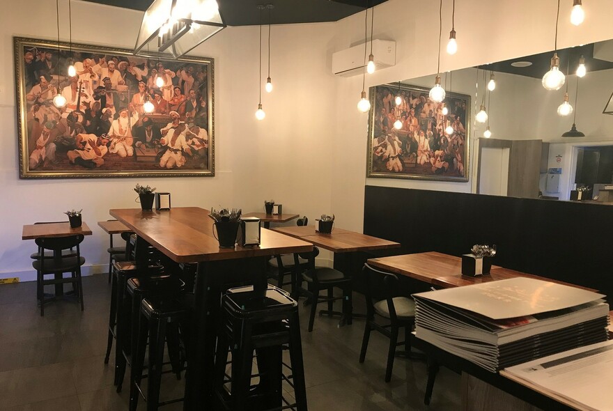 Cafe interior with artwork and mirrored wall, pendant lighting and tables.