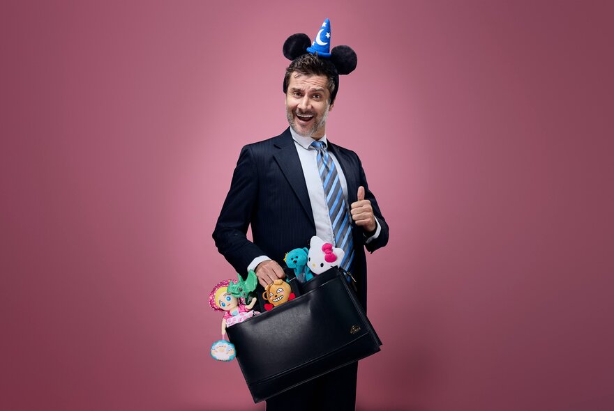 Children's performer, Mr Snotbottom, posing with thumbs up in a suit and Mickey Mouse ears, holding a doctors bag filled with small creatures.