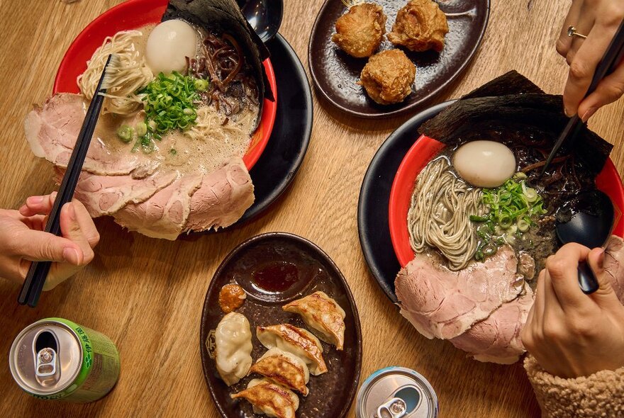 Bowls or ramen noodles with slices of pork. There are also plates of dumplings and fried chicken.