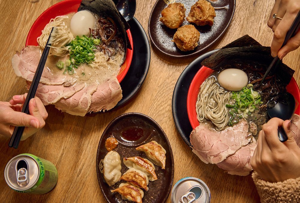 Bowls or ramen noodles with slices of pork. There are also plates of dumplings and fried chicken. 