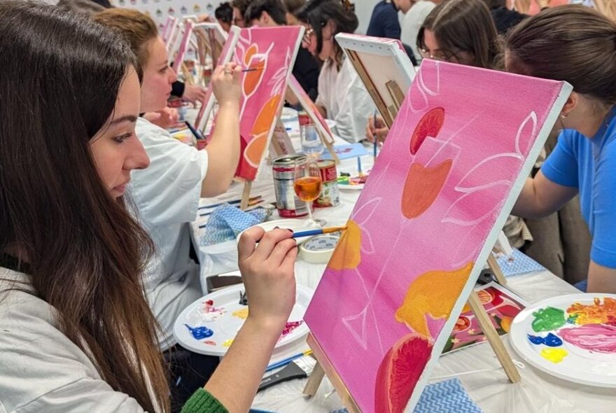 Workshop participants painting on small canvases, at a long workshop table.