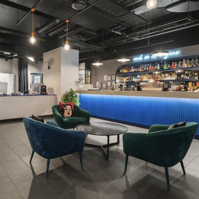 The interior of a hotel lobby with a blue reception desk and blue and green velvet armchairs.