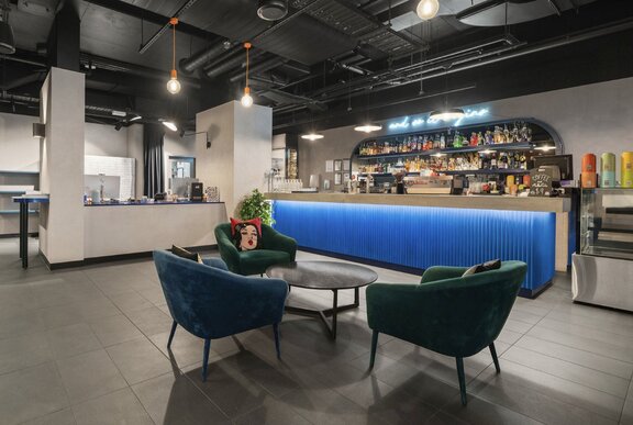 The interior of a hotel lobby with a blue reception desk and blue and green velvet armchairs.