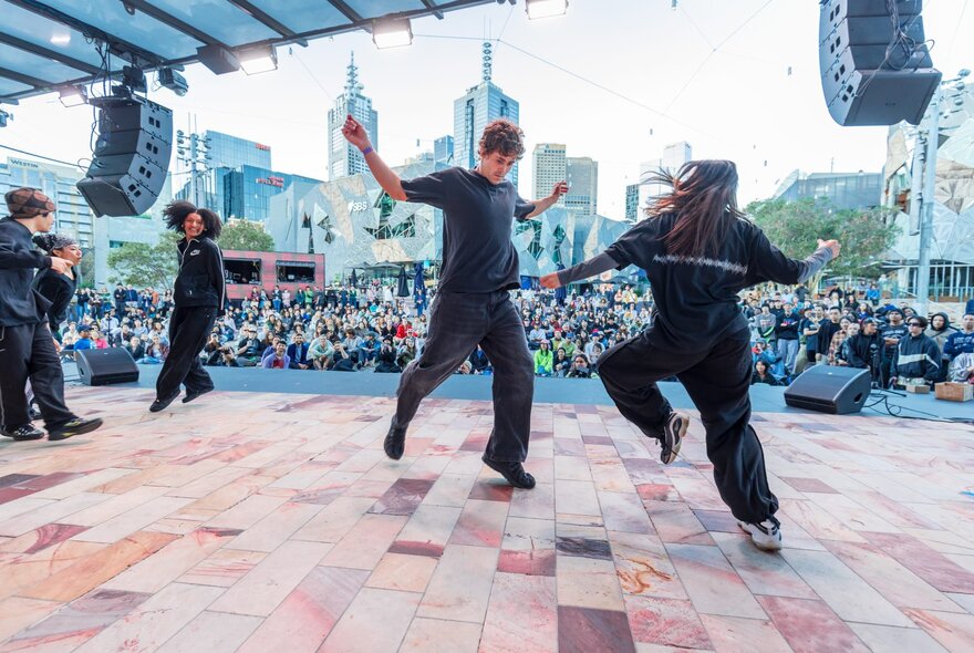 Three hip hop dancers battling on stage at Melbourne's Fed Square, a large crowd looking on in the background.